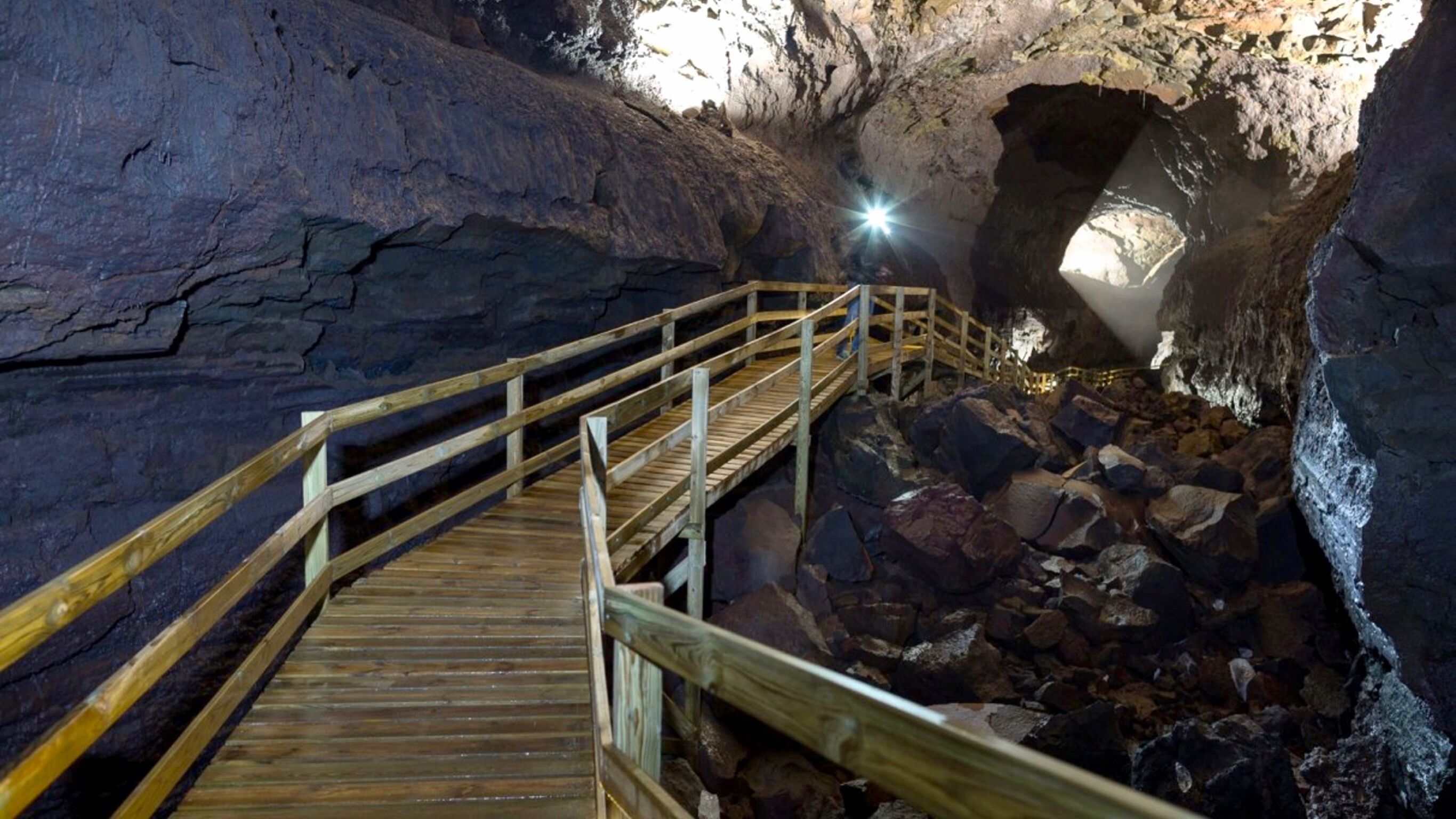 Una escalera de madera que conduce a una cueva, con una fuente de luz natural en la parte superior.