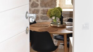 A dining area with a stone wall, a wooden table, black chairs, and a black pendant light. - Charming stone house in Cavtat old town (Cavtat)