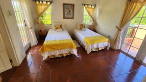 A room with two beds, each with a yellow bedspread, a painting on the wall, and a window with curtains.