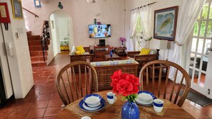A dining area with a wooden table set for four, a television mounted on the wall, and a staircase leading to an upper level.