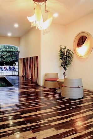 A spacious room with a wooden floor, a hanging light fixture, a round mirror, and a potted plant.