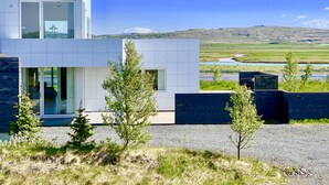 Un bâtiment moderne à deux étages, doté de grandes fenêtres et offrant une vue sur une rivière et des collines en arrière-plan.
