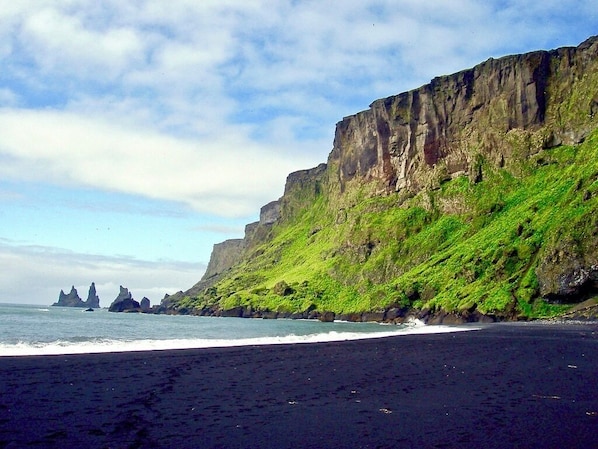 A beach with a black sand shore, green cliffs, and rock formations in the distance. - Brún Golden Circle Villa, Private Hot Tub & River Views, Walk to Laugarás Lagoon (Selfoss)