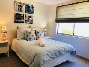 A bedroom with a large bed, two bedside tables, a window with blinds, and wall art.