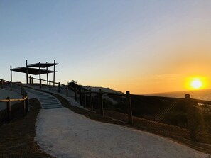 A snow-covered pathway leading to a beach with a fence and a covered structure.