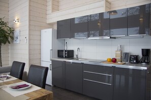 A modern kitchen with grey cabinets, a white refrigerator, and a wooden dining table with chairs. - Beautiful mini villa right on the lakeside (Uro)