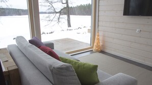 Una sala de estar moderna con un sofá gris, cojines verdes y rojos, y vistas a un paisaje nevado a través de amplios ventanales.