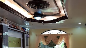 Ein Wohnzimmer mit Deckenventilator, Fernseher, einer Sofagarnitur und einem Kamin.