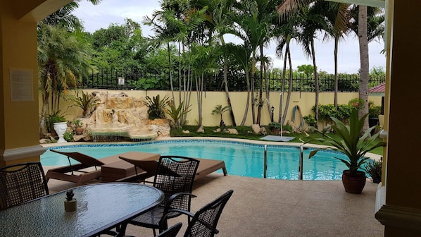 A pool area with a waterfall feature, surrounded by palm trees and a stone wall. - House With Nice Garden And Big Private Pool For Rent and secure power situation. (Cebu)