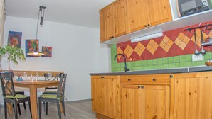 Une cuisine avec des meubles en bois, un four à micro-ondes, une table à manger avec des chaises et des carreaux colorés sur le mur derrière l’évier ou la cuisinière.