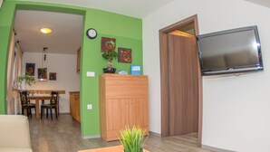Un salon avec un téléviseur, des meubles en bois, un coin repas avec des chaises et une plante en pot.