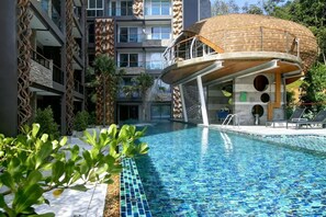 Une piscine au design moderne, entourée d’immeubles à plusieurs étages dotés de balcons et d’une structure sphérique unique.
