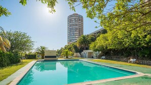 A rectangular swimming pool with a greenish-blue tint, surrounded by a low stone wall and lush greenery. - Iconic Architecture With Sweeping Mountain Views! (Cape Town)