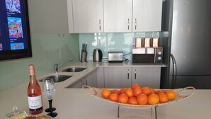 A kitchen with a stainless steel refrigerator, a microwave, and a toaster. There are two sinks, a wine bottle, and a basket of oranges on the counter. - Iconic Architecture With Sweeping Mountain Views! (Cape Town)
