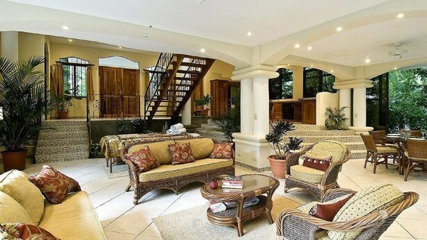 A spacious living area with a sofa, chairs, and a coffee table. There is a staircase leading to an upper level. - Enchanted Home 7  bedroom home. (Quepos/Manuel Antonio)