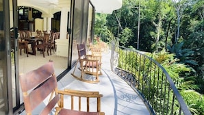 A balcony with wooden chairs and tables, surrounded by lush greenery. - Enchanted Home 7  bedroom home. (Quepos/Manuel Antonio)