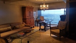 Un salon comprenant un canapé, une table basse et des fauteuils, un meuble en bois et une vue sur l’océan.