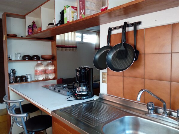 A compact kitchen with a gas stove, a coffee maker, and hanging pots.