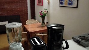 A kitchen with a blender, toaster, and coffee maker on the counter. There is a brick wall, a framed picture, and a vase with flowers on the wall. - Casa La Joya in Down Town- Santo Domingo Church (Oaxaca)