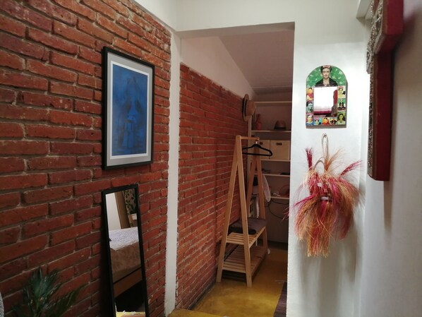 A narrow hallway with a brick wall, a wooden ladder, a mirror, and a hanging plant.