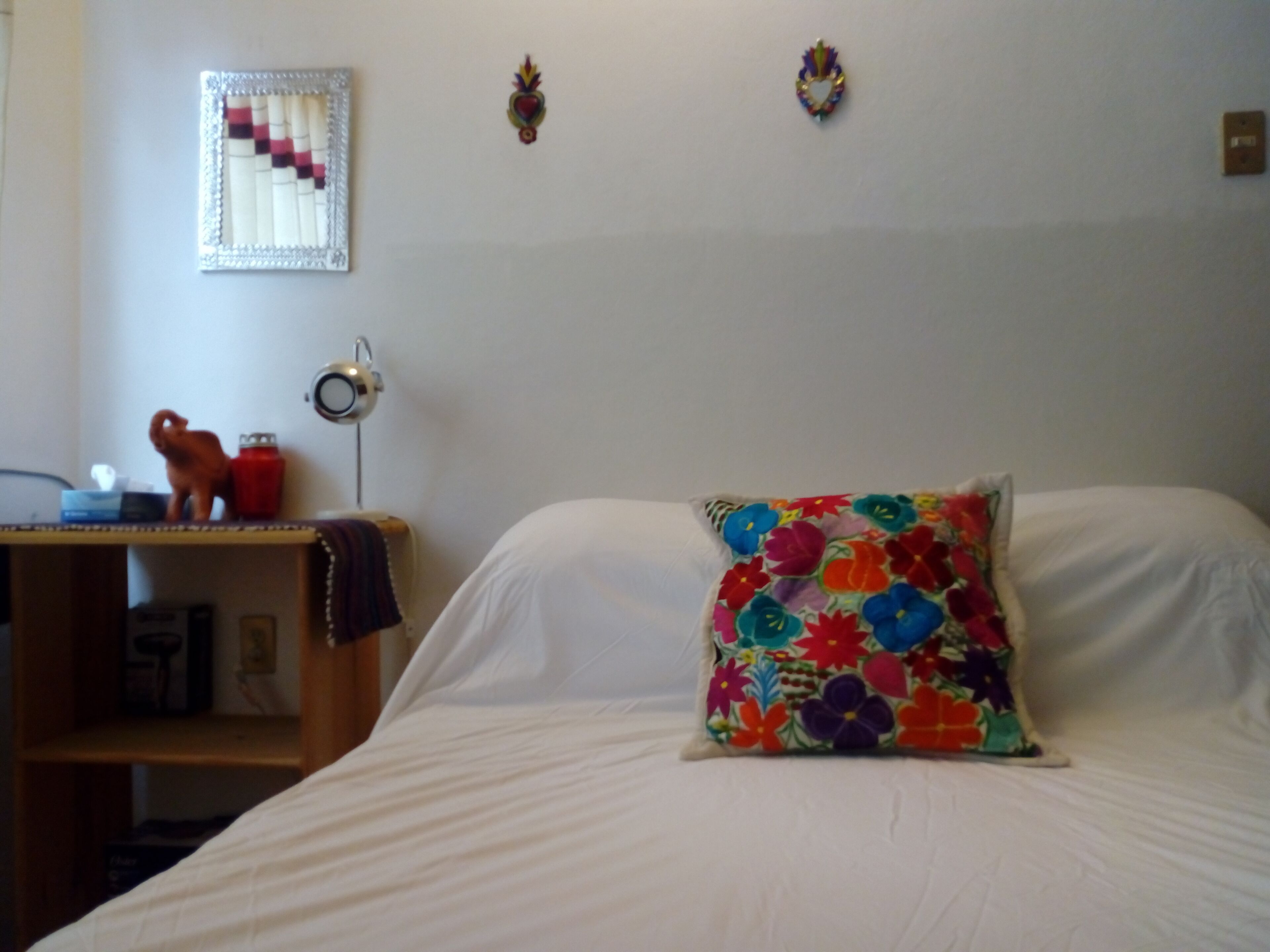 Une chambre à coucher avec un lit, un bureau doté d’une lampe et un coussin aux couleurs vives.
