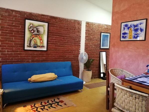 A living room with a blue sofa, a wicker chair, a small table, and a fan.