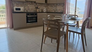 A modern kitchen with a dining area, featuring a tiled backsplash, stainless steel appliances, and a large window with curtains.