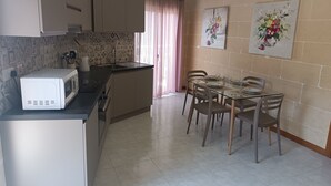 A compact kitchen with a microwave, a sink, and a dining area with chairs and a glass table.