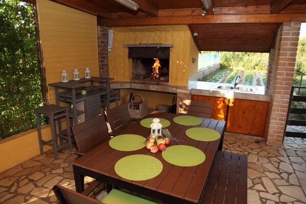 An outdoor patio with a brick oven, a sink, and a table set with green placemats and apples.