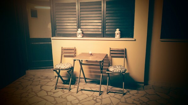 Uma pequena área de refeições com uma mesa e duas cadeiras, uma janela com persianas e um chão de azulejos.