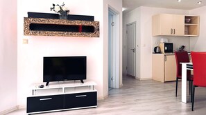 A modern living room with a flat-screen TV, a decorative mirror, and a dining area with a red chair.