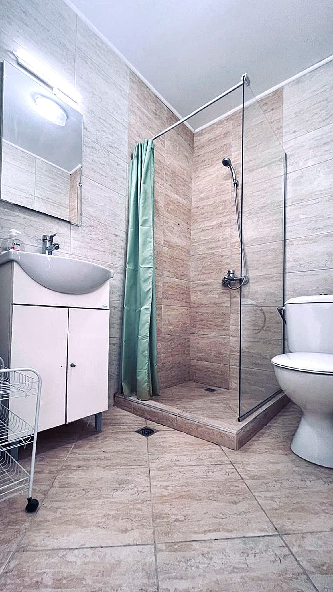 A bathroom with a shower, toilet, sink, and mirror.