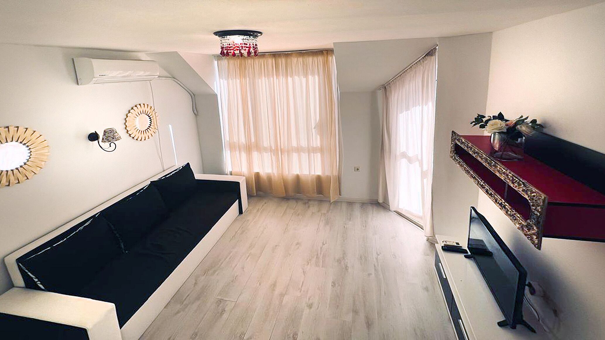 Un salon moderne avec un canapé noir, un téléviseur à écran plat et un miroir décoratif au mur.