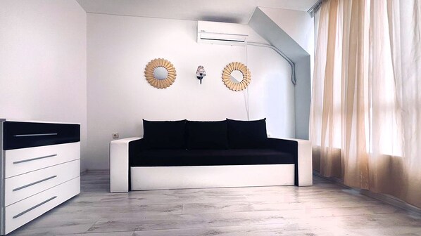 A modern bedroom with a white sofa, a bedside table, a wardrobe, and a ceiling-mounted air conditioner.