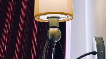 Een wandlamp met een cilindrische lampenkap en een verstelbare arm, bevestigd aan een muur met een rood gordijn op de achtergrond.