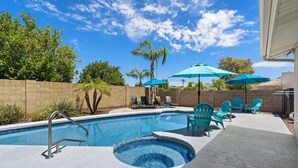 A swimming pool with a hot tub, surrounded by chairs and umbrellas, with a brick wall and trees in the background. - L2 EV, Modern Home With Putting Green, Pool, Spa, Pet Friendly, Split Floorplan (Scottsdale)