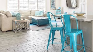 A spacious living area with a sofa, ottoman, and two blue chairs. A dining table with chairs is positioned near a kitchen island. - L2 EV, Modern Home With Putting Green, Pool, Spa, Pet Friendly, Split Floorplan (Scottsdale)