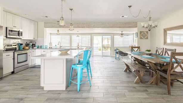 A spacious kitchen with white cabinetry, a central island, blue bar stools, and a wooden dining table with chairs. - L2 EV, Modern Home With Putting Green, Pool, Spa, Pet Friendly, Split Floorplan (Scottsdale)
