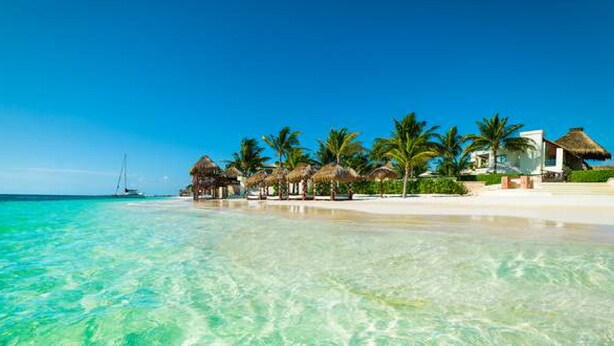 A beach with clear turquoise water, palm trees, and thatched-roof structures. - Clean spacious apartment w/ pool. Central Cancun 5 mins from beach (Cancún)