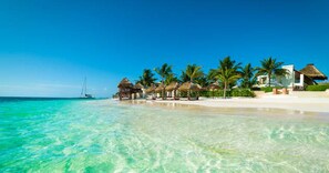 A beach with clear turquoise water, palm trees, and thatched-roof structures.