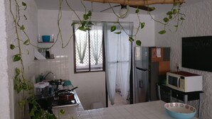 A kitchen with white tiles, a stove, a refrigerator, and a microwave. There are plants hanging from the ceiling and a chalkboard with writing on it. - Clean spacious apartment w/ pool. Central Cancun 5 mins from beach (Cancún)