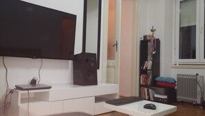 A modern living room with a flat-screen TV, a white entertainment unit, a bookshelf, and a radiator.