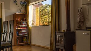 A room with a wooden bookshelf, a window with a view of trees, a small stove, and a white refrigerator. - Beautiful house with garden in historic center Cusco (Cusco)