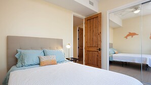 Une chambre avec un grand lit, une table de chevet et une lampe. On y trouve une porte en bois et une petite table avec une lampe.