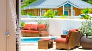 A pool area with outdoor furniture, a house in the background, and a water feature.