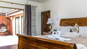 A bedroom with a wooden bed, a nightstand with a lamp, a window with curtains, and a hanging chair. - Three Bedroom Samaan Villa (Bon Accord)