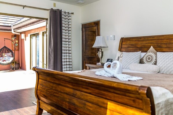 Un dormitorio con una cama de madera, una mesita de noche con lámpara, una ventana con cortinas y un sillón colgante.