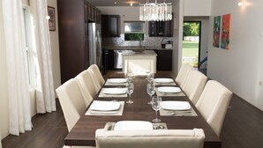 A dining room with a long table set for six, surrounded by cushioned chairs. - Three Bedroom Samaan Villa (Bon Accord)