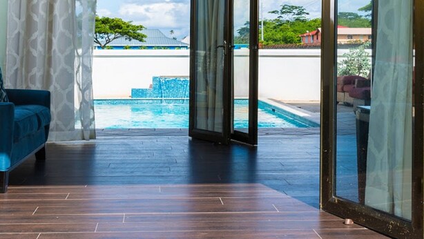 A room with a view of a swimming pool, a blue sofa, and a glass door leading outside. - Three Bedroom Samaan Villa (Bon Accord)
