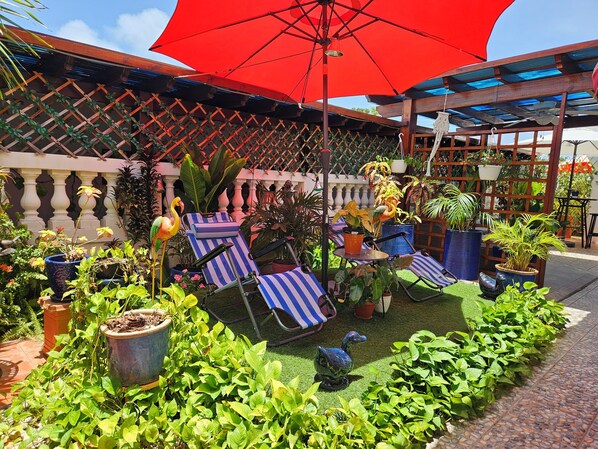 A patio area with lounge chairs, potted plants, and a large red umbrella.